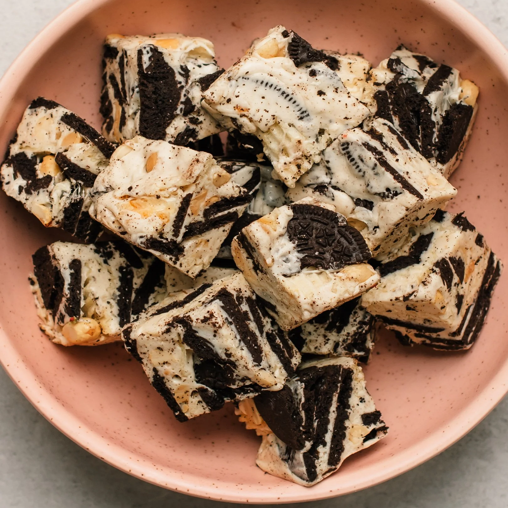 Creamy Oreo fudge squares with crushed cookies and peanuts in a pink bowl